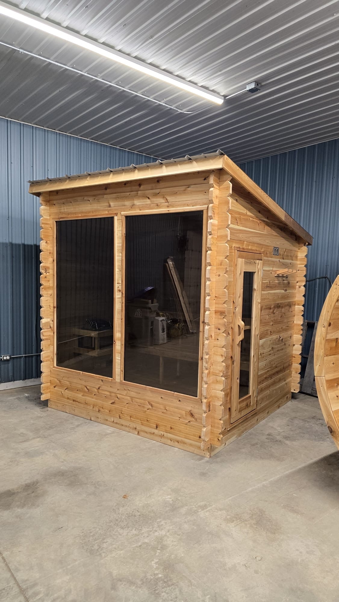 Wooden lean to sauna inside a warehouse with concrete floor and blue walls.