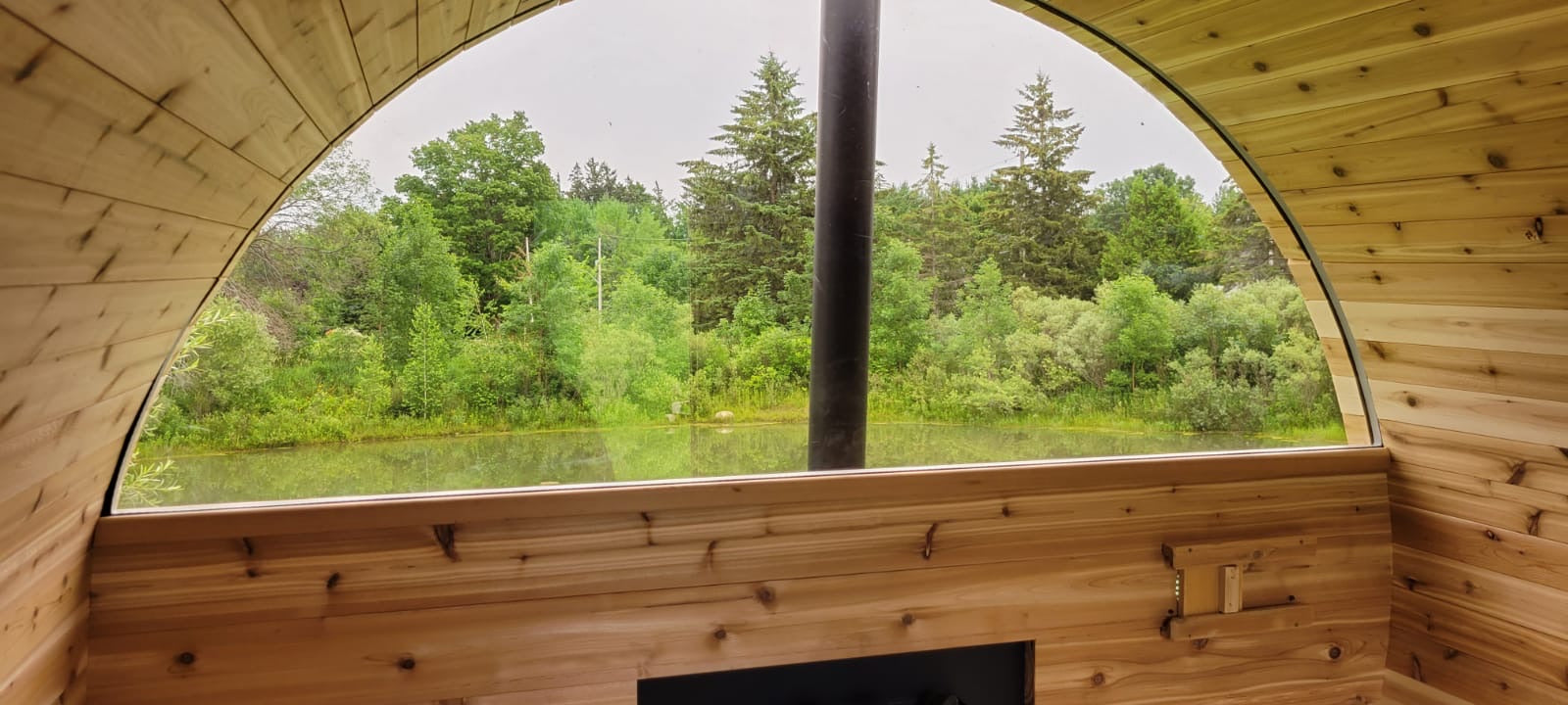 Wooden interior of a sauna with a large window view of green trees and water.