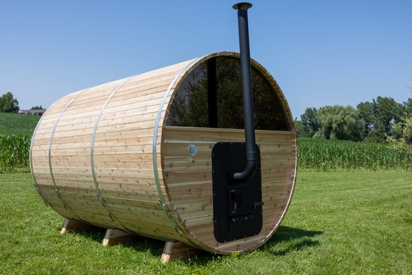 Wooden barrel-shaped sauna with a black exhaust pipe on a grassy field.