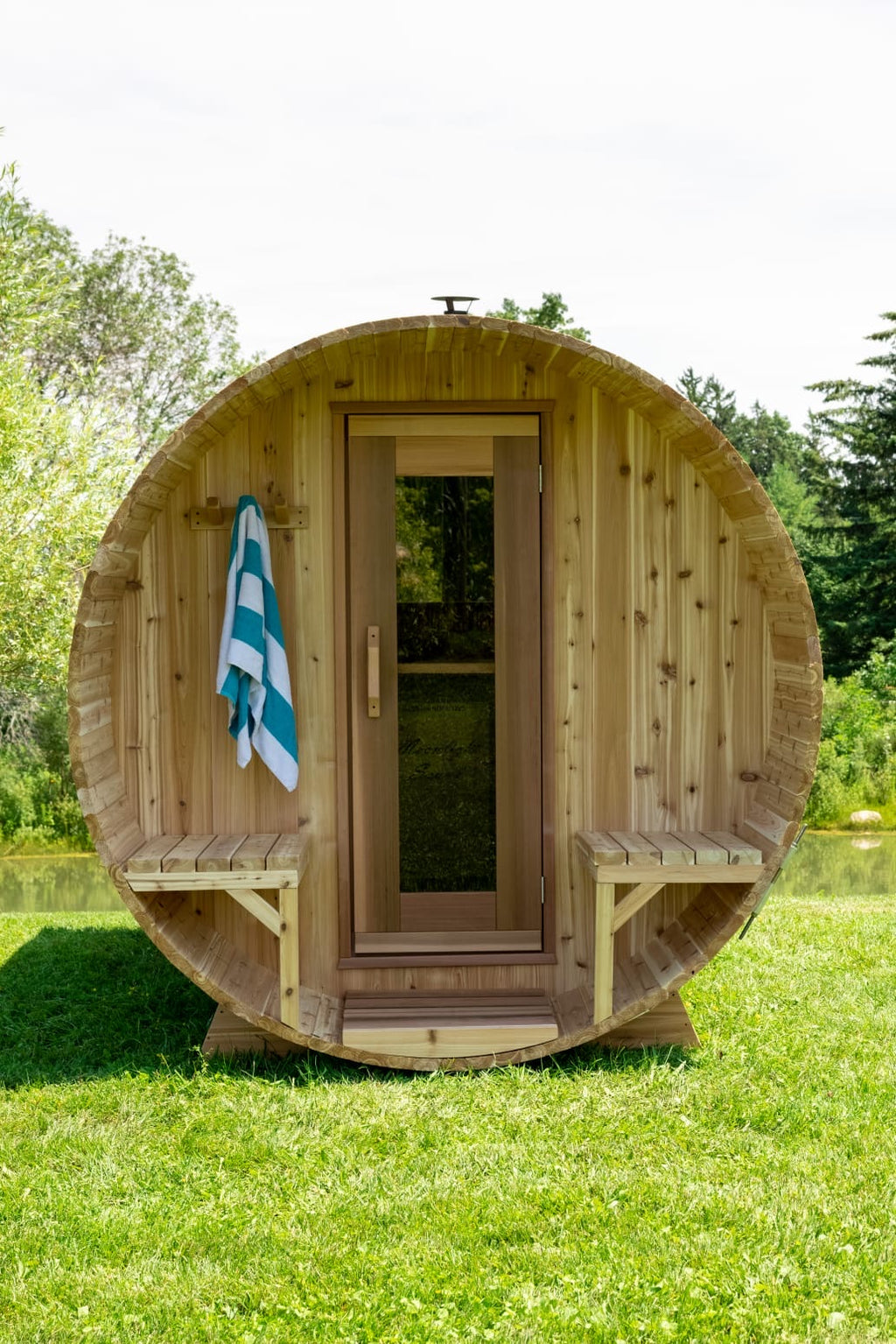 Wooden barrel-shaped sauna with a towel hanging on a grassy area