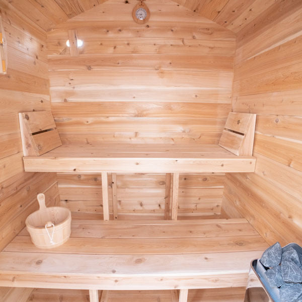 Wooden sauna with benches and a bucket on a wooden floor.
