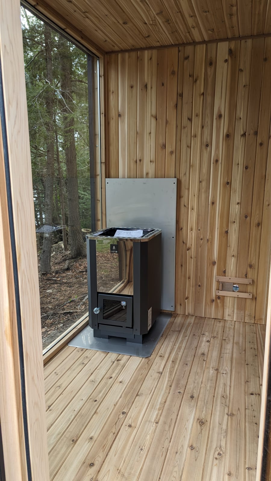 Wooden sauna cabin interior with a wood stove and view of trees outside
