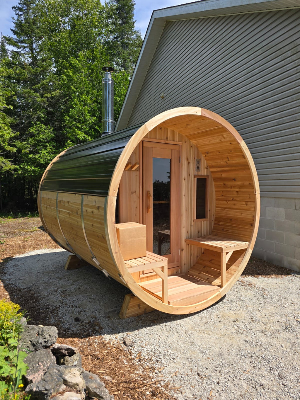 Wooden barrel-shaped sauna outside a building with trees in the background