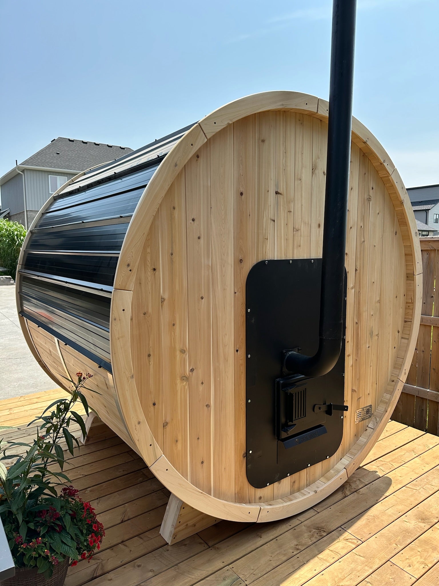 Wooden barrel sauna with an exterior feb wood heater on a wooden deck