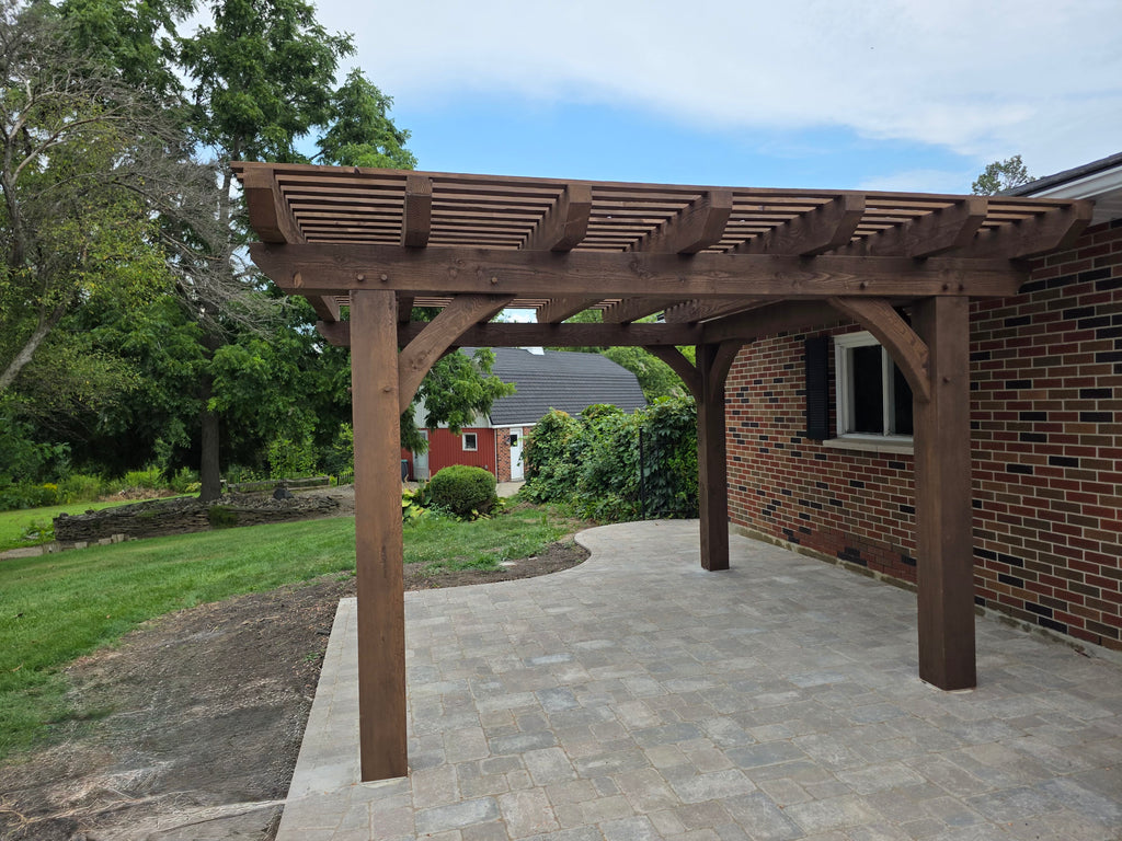 Wooden pergola attached to a brick building with a garden and house in the background.