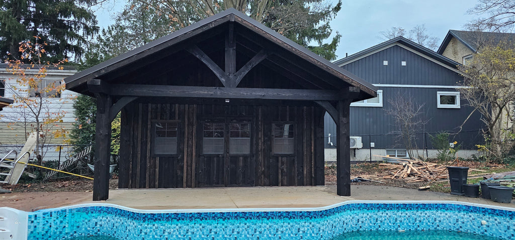 Wooden pool house next to a swimming pool with houses and trees in the background