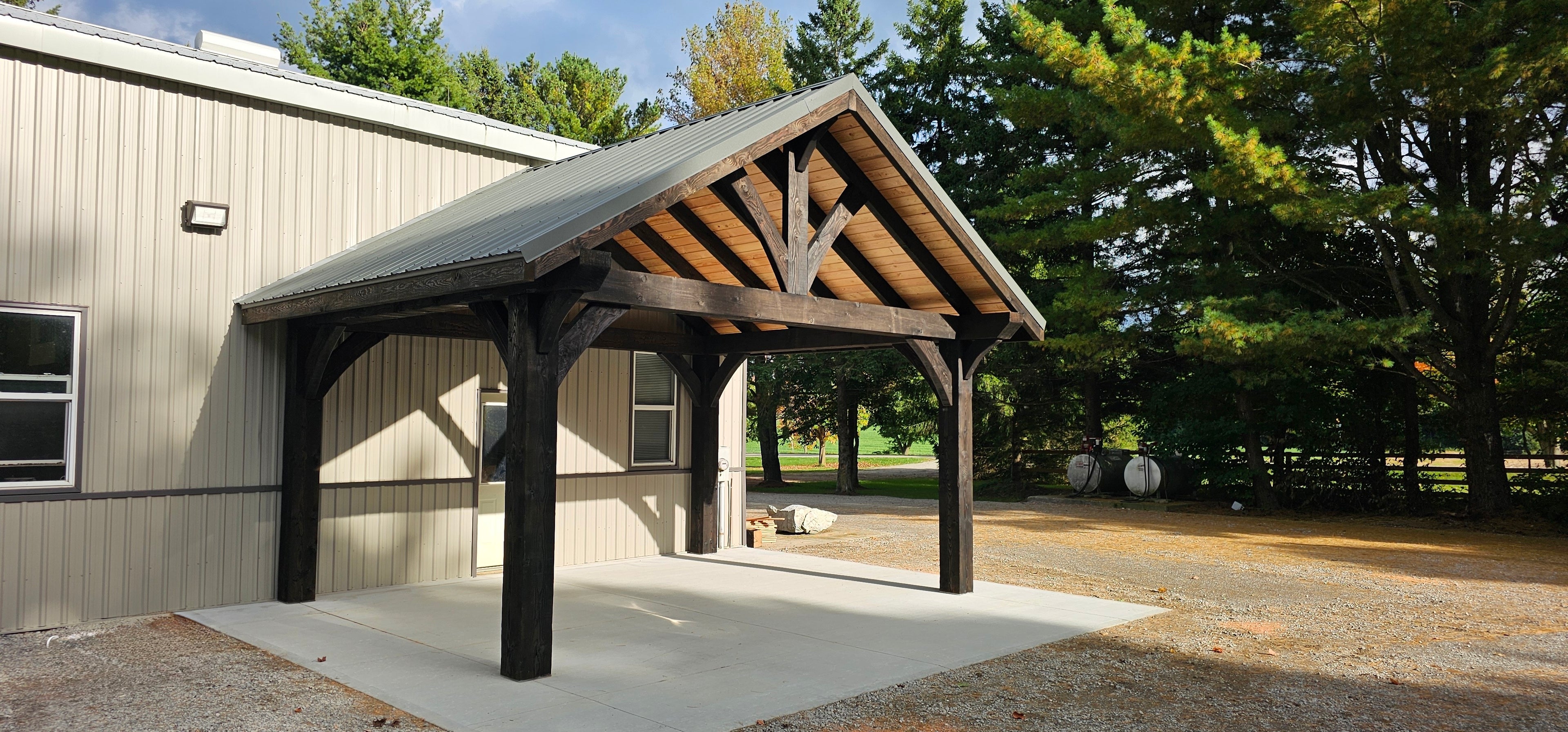 Wooden carport attached to a building with trees in the background