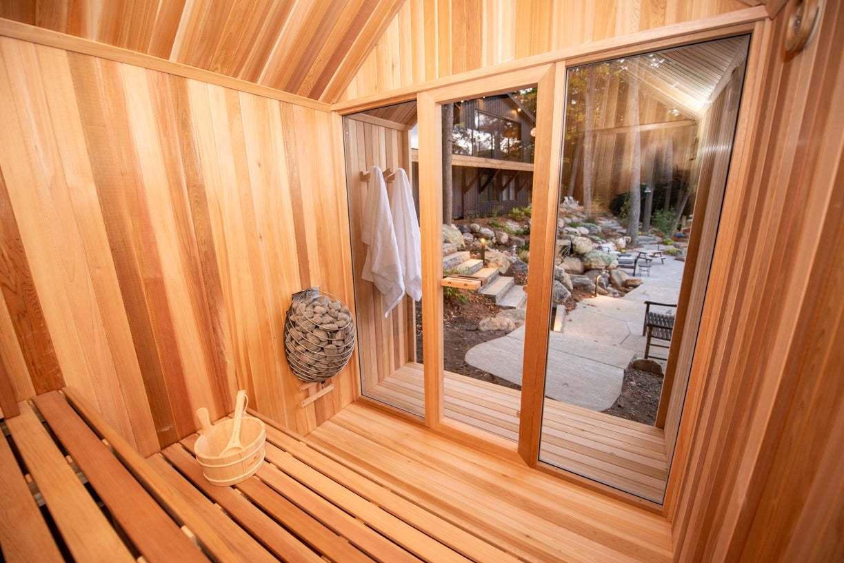 Wooden sauna interior with a view of a garden outside the window.