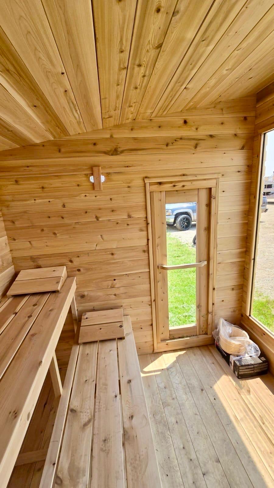 Wooden lean to sauna interior with benches and a door leading outside.